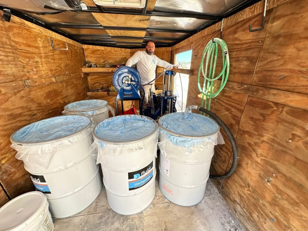 Fluid Applied Roofing FiberSeal basecoat drums and spray rig for a commercial roof restoration